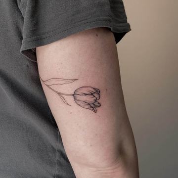 Minimal linework tulip tattoo on the upper arm